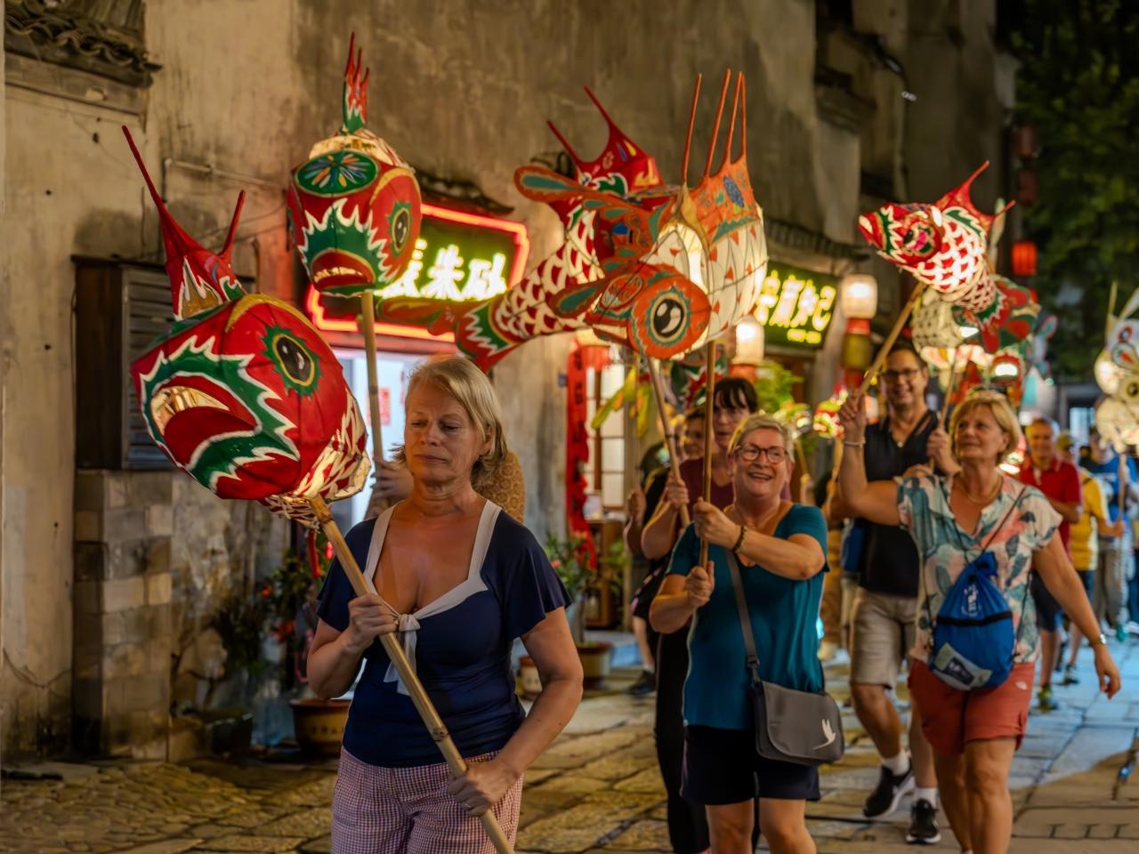 Travelers participating in festive fish lantern parade in ancient town